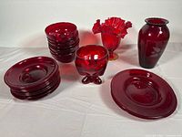 Group view of all ruby red glass items: stacked bowls, plates, three vases