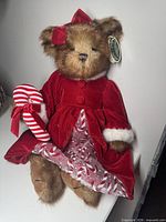 Full view of dressed teddy bear seated, showing dress, candy cane, bow