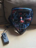 Front of mask showing blue EL wire pattern and red splatter, battery pack attached