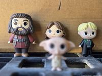 Front view of four Funko vinyl figures Dobby (blurred foreground), Hagrid, female Hogwarts student, Draco