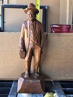 Full view of wooden male figurine with basket, tape shows height