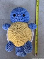 Front view of crocheted Squirtle plush alongside measuring tape showing height