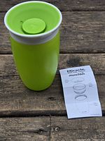 Assembled green trainer cup with collar and valve inserted, instruction sheet alongside