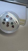 Circular gem jar showing nine round faceted sapphires of varied colours