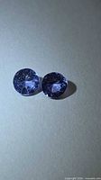 Two round purple-blue Tanzanite stones on neutral background