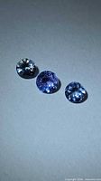 Three round faceted Tanzanite gemstones on neutral background