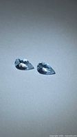 Two pear-cut aquamarine gemstones on light surface