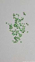 Scatter of small round green tsavorite garnet stones on neutral background
