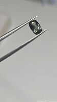 Oval platinum green sapphire held in tweezers, side view shows luster