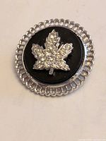 Front view showing rhinestone maple leaf on black center with silver openwork border