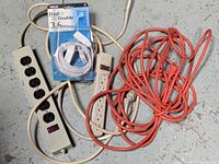 All electrical items together: metal power bar, plastic power strip, orange extension cord, sealed white cable