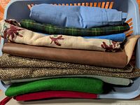 Stack of assorted fabrics in basket, top to bottom blue chambray to red fleece