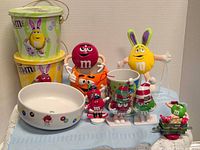 Group shot showing all M&M items including buckets, bowl, dispenser, mug, plush and ornaments