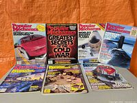 All eight Popular Mechanics magazines arranged, four standing and four lying flat