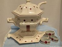 Full view of soup tureen on underplate with ladle inserted and napkin rings in foreground