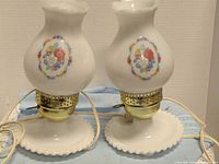 Front view of both milk glass lamps showing hobnail bases, brass sockets and floral shades