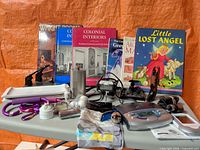 Overview of lot showing books, movie light, tray, stethoscope, flask, figurine and electronics on folding table