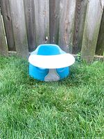 Front view of blue/teal Bumbo seat with white tray attached, on grass