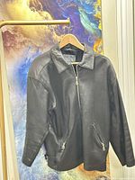 Front view of black leather jacket on hanger showing zipper closure and pockets