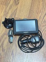 GPS unit with mount, car charger and USB cable on wooden surface