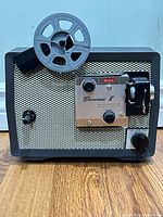 Front view of projector showing reel arm, grille, control panel and knobs