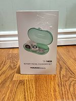 Front of product box showing teal cleanser in case with brush heads