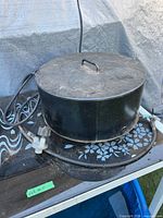 Cylindrical steel fire pit burner with lid, hose and regulator visible