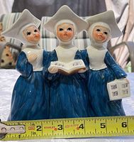 Front view of three singing nuns figurine with tape measure showing height