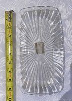 Top view of rectangular clear glass tray showing starburst pattern and tape measure indicating about 10 inches length