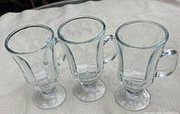 Three clear glass footed mugs front view