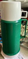 Full view of green and white Thermos flask with handle and cup lid attached
