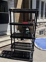 Front view of five-shelf black plastic shelving unit assembled outdoors