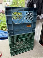 Two stacked plastic milk crates, blue and green, showing brand markings and wear