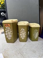 Front view of three olive canisters with cream lids showing floral graphics