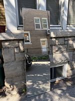 Full view of mirrored door leaning against stone wall