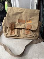 Front view showing flap, pockets, leather straps, logo