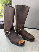 Front angle of both brown leather harness boots showing toe stitching and brass hardware