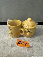 Front view of yellow ceramic creamer and sugar bowl with cartoon faces, plastic wrap intact