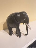 Left-side view of wooden elephant figurine displaying tusks, eye inlay and overall form