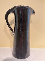 Full side view of tall black ceramic pitcher showing handle and overall form