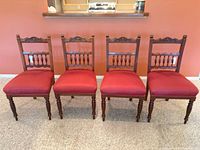 Front view of four matching carved wooden chairs with red seats