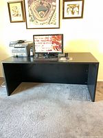 Front view of black rectangular desk with computer and printer on top