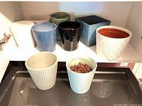 Cabinet shelf showing eight assorted ceramic planters