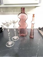 Group shot of all four glass pieces: purple wavy vase, purple decanter with stopper, two clear twisted-stem candlesticks