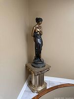 Full view of bronze female sculpture on pedestal stand in corner
