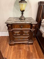 Front view of first nightstand showing marble top, drawers, hardware, carved details