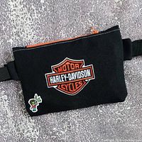 Full view of black fanny pack showing Harley-Davidson patch, orange zipper, strap