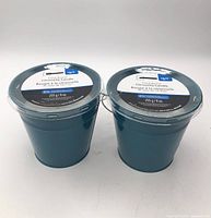 Front view of both teal bucket citronella candles with lids and labels