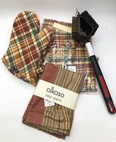 Group shot of all items: apron in package, oven mitt, table linens bundle, grill brush