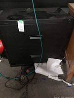 front view of black metal two-drawer filing cabinet, showing handles and overall condition